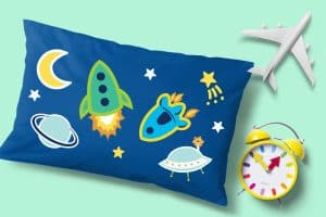 A pillow with a space theme design, next to an alarm clock and an airplane toy.