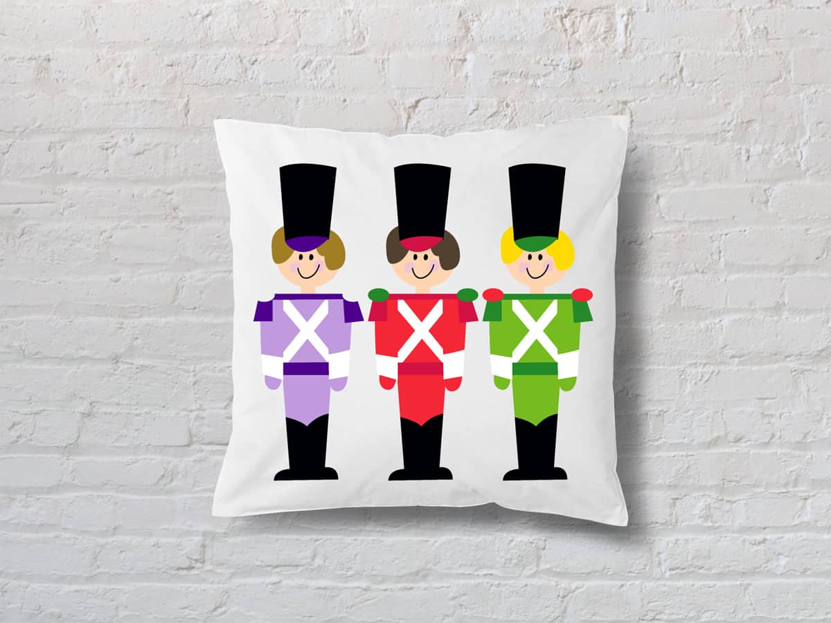 A white cushion with an illustration of three Nutcracker figures against a white wall
