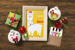 From above, a wood frame with a cute Christmas illustration is surrounded by decorations on a wood floor.