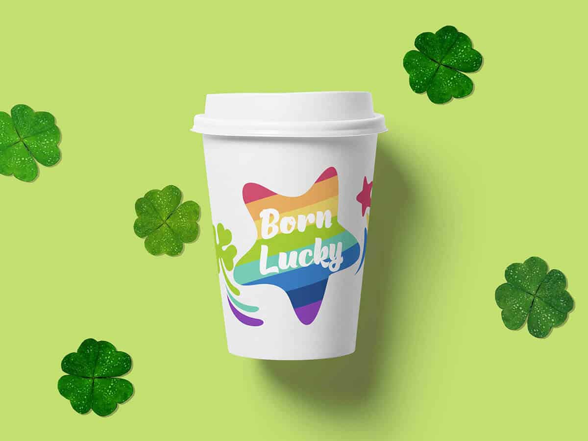 A white paper cup with "Born Lucky" written on a rainbow star