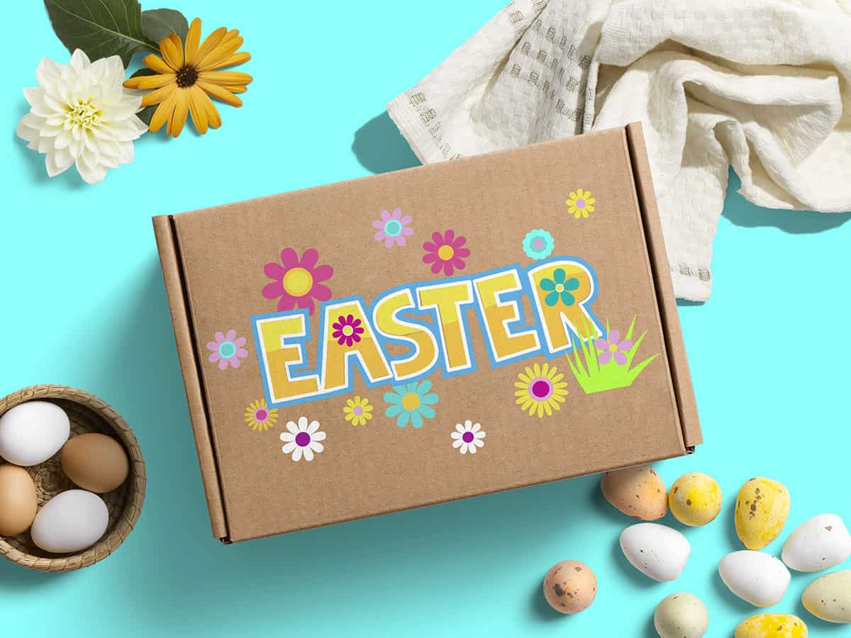 A top view of a cardboard with an Easter illustration, surrounded by flowers and eggs on a turquoise background