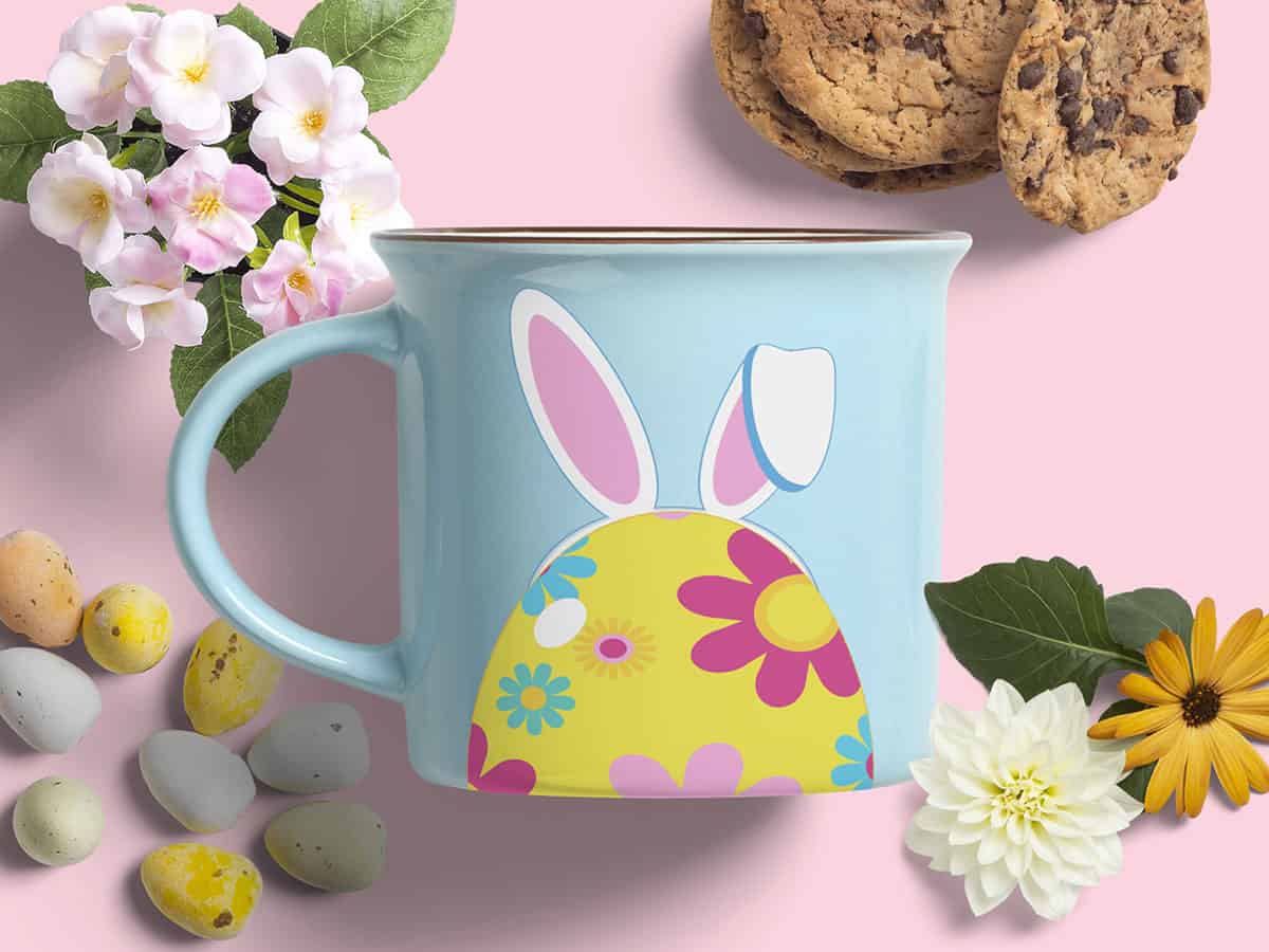 Top view of a blue mug with an Easter egg with a big bunny ear illustration surrounded by flowers and eggs