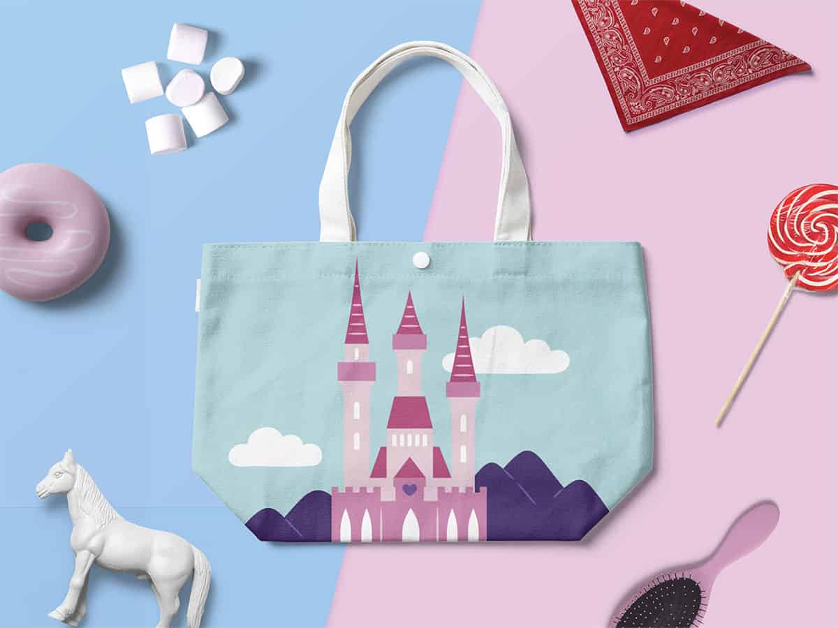 Kids' tote bag with castle design surrounded by a horse figure, a pink donut, marshmallows, and a red bandana on a blue and pink split background.